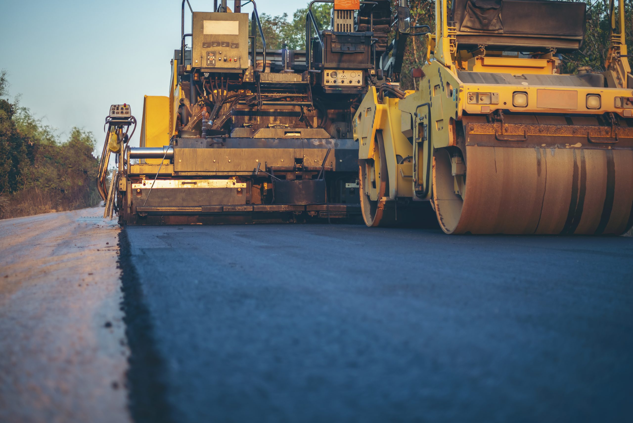 Yellow asphalt paving equipment rolling out freshly-installed asphalt