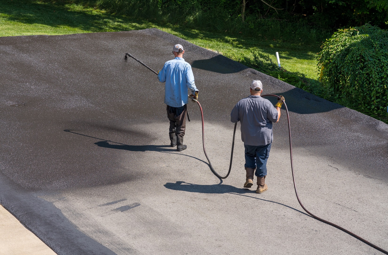 Workers applying blacktop sealer to asphalt street